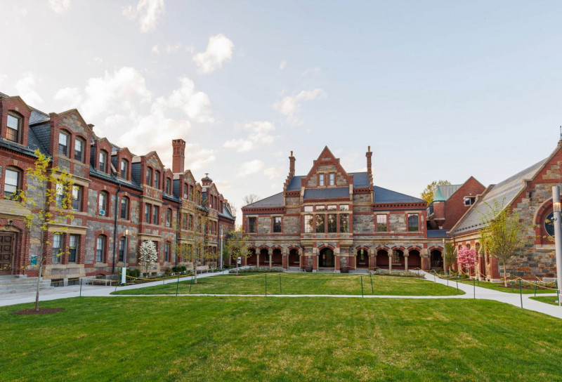 A picturesque view of historic university buildings and a green lawn, the